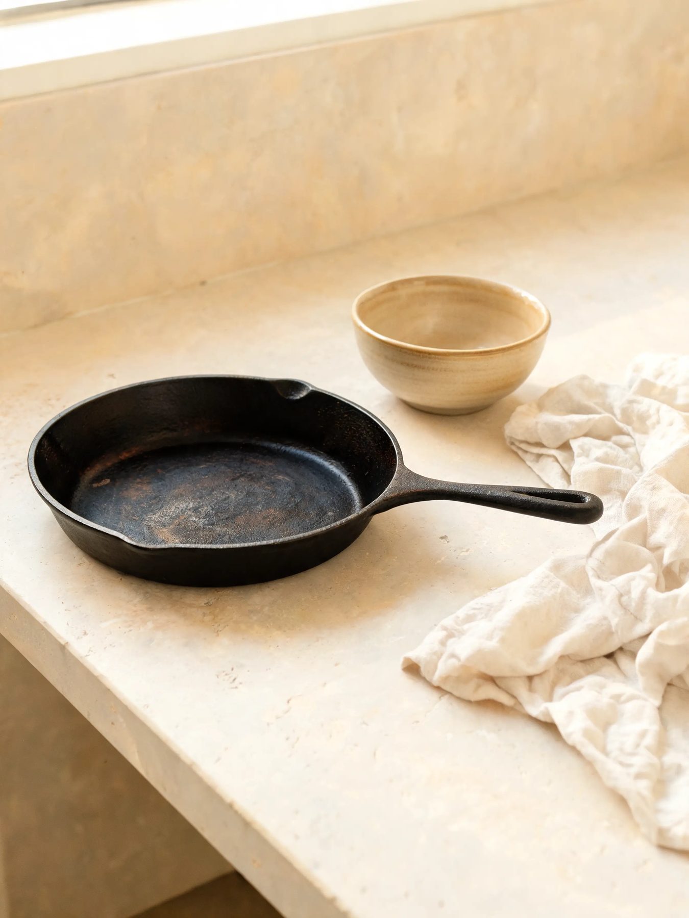 Seasoned skillet and glazed stoneware bowl on a limestone counter